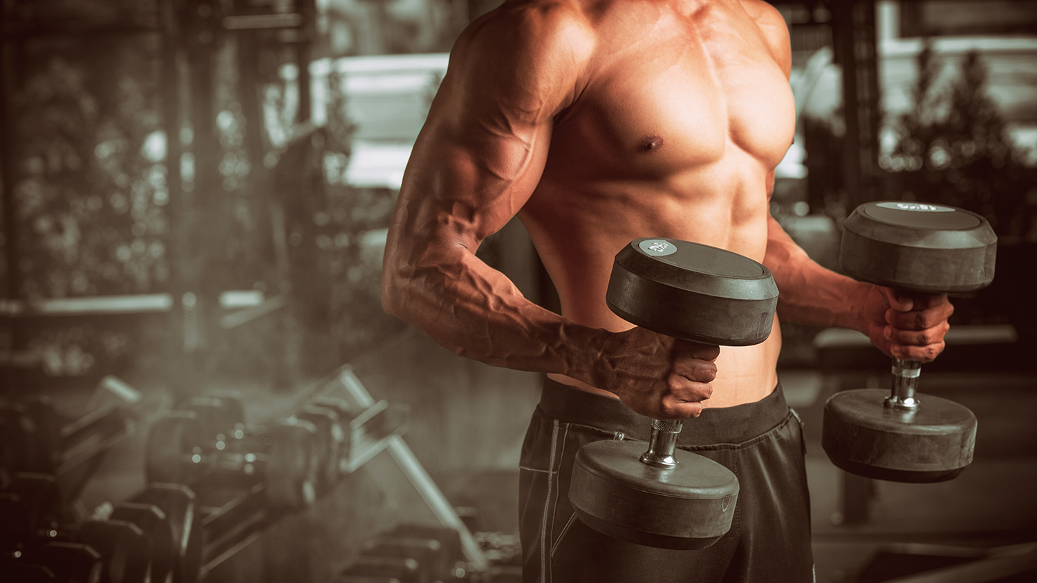 male in gym flexing biceps while holding dumbells