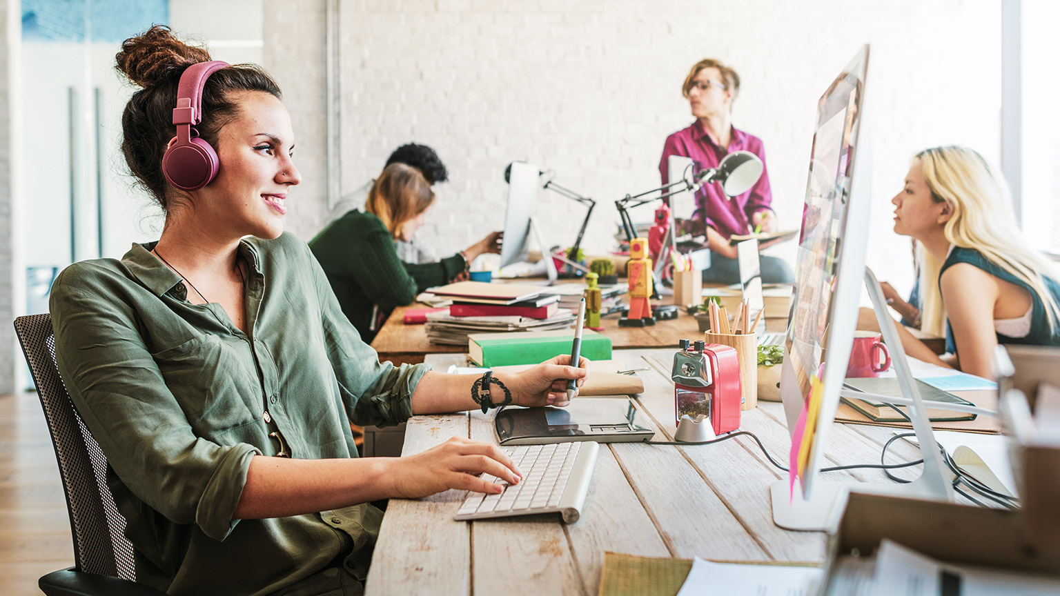 Smiling designer working at a computer with colleagues in the background