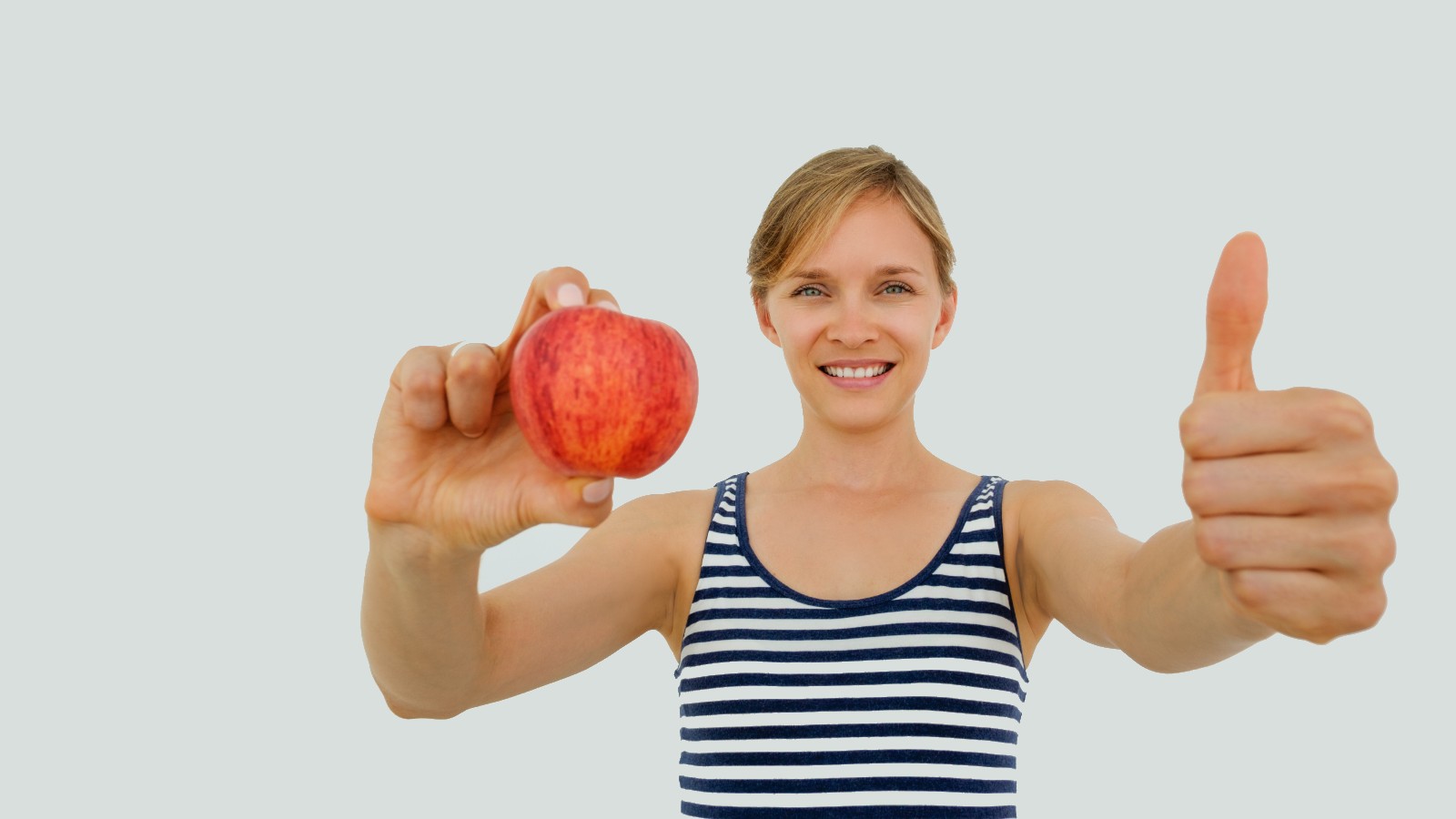 Woman in fitness attire holding and apple and giving a thumb up