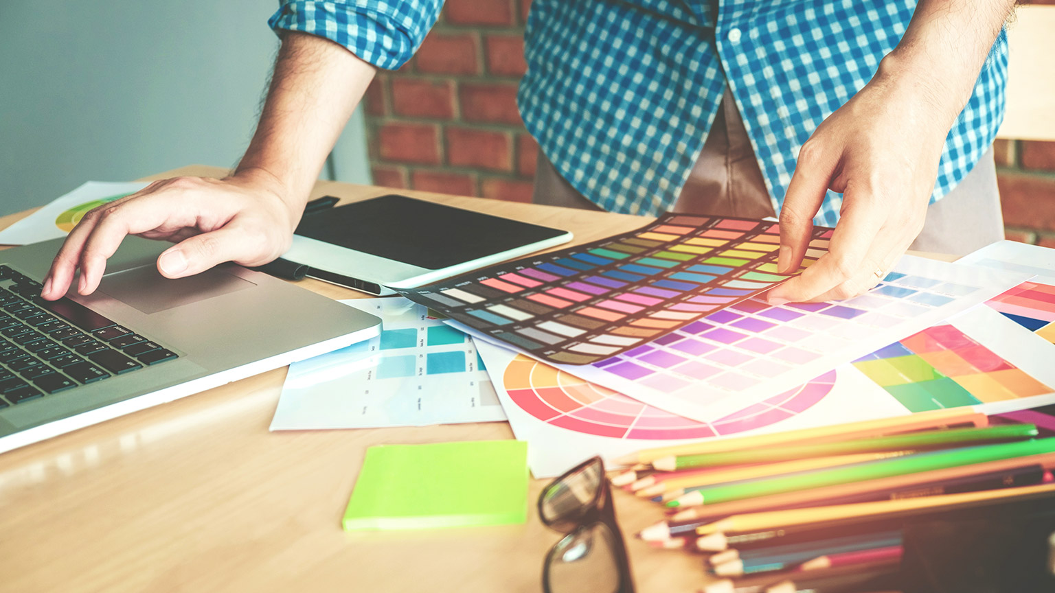 Designer at desk using a laptop with colour samples on the desk