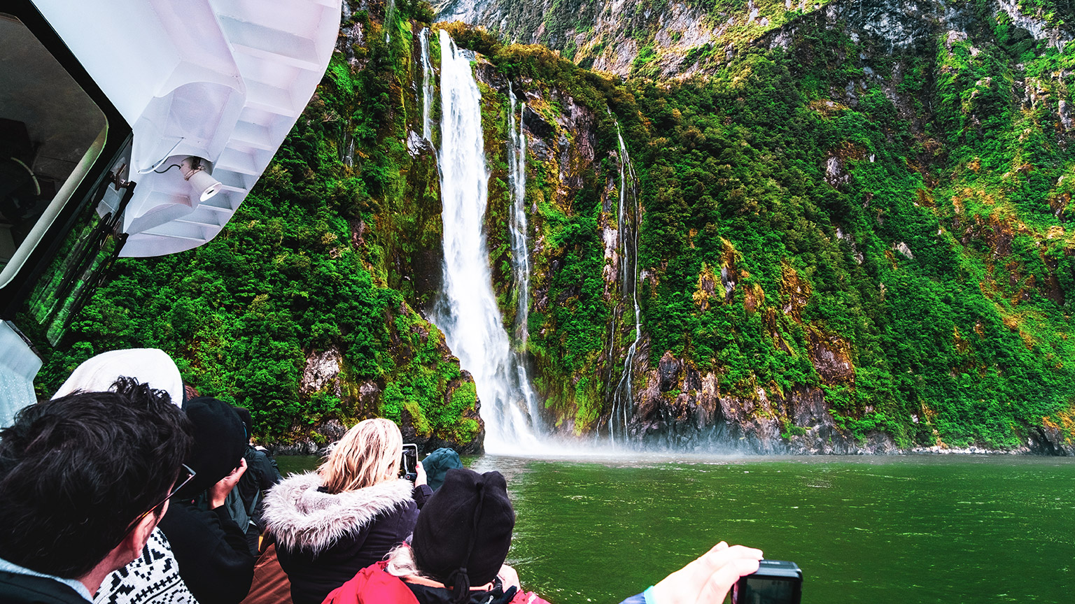 Group of tourists on a boat viewing a waterfall near Milford Sound