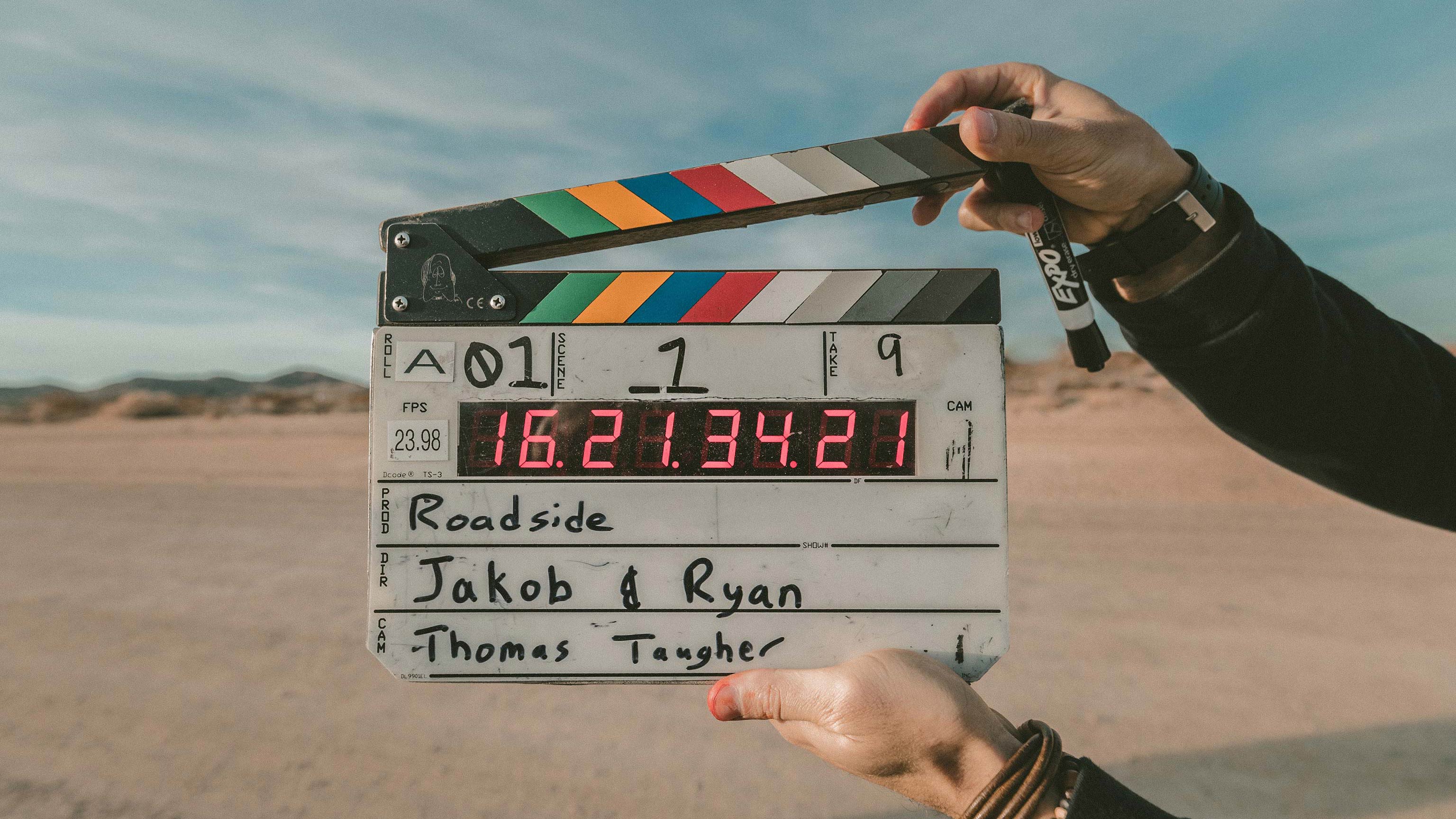 A man holding a clapboard in front of a scene