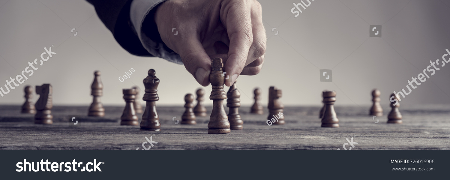 A human hand wearing business suit moving dark King chess piece at table, toned retro effect