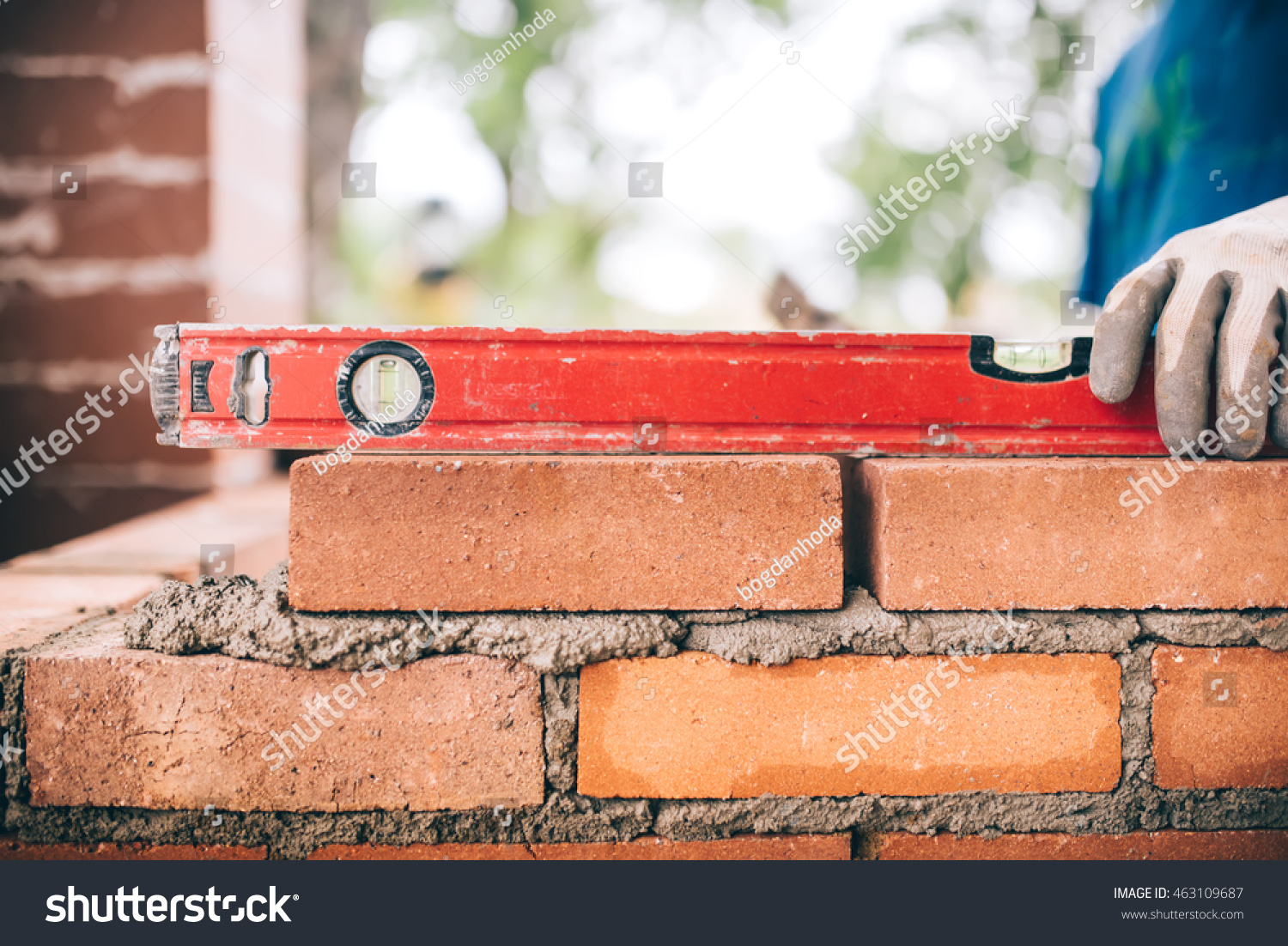  463109687 construction worker, bricklayer laying bricks and creating walls. Detail of level tool