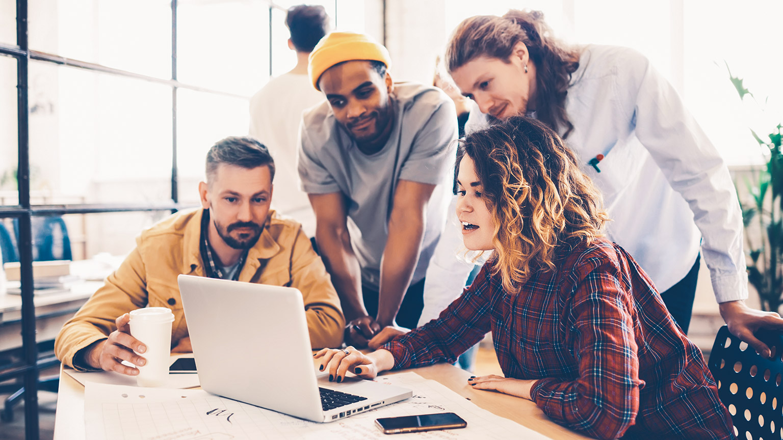 Group of young designers sitting around a table discussing a project on a laptop