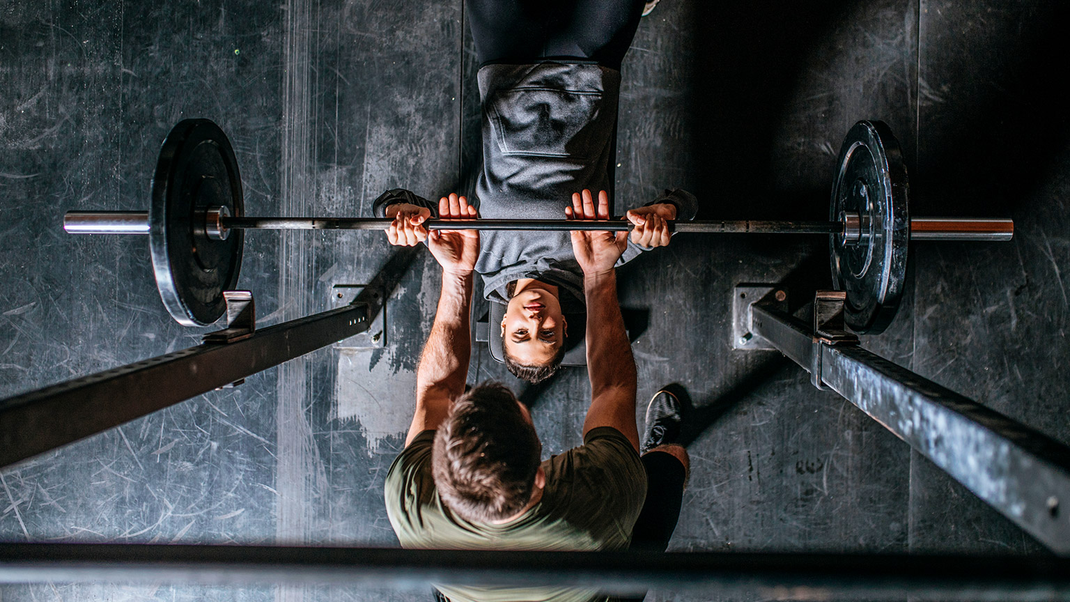 Top down view of male trainer assisting client on weight bench