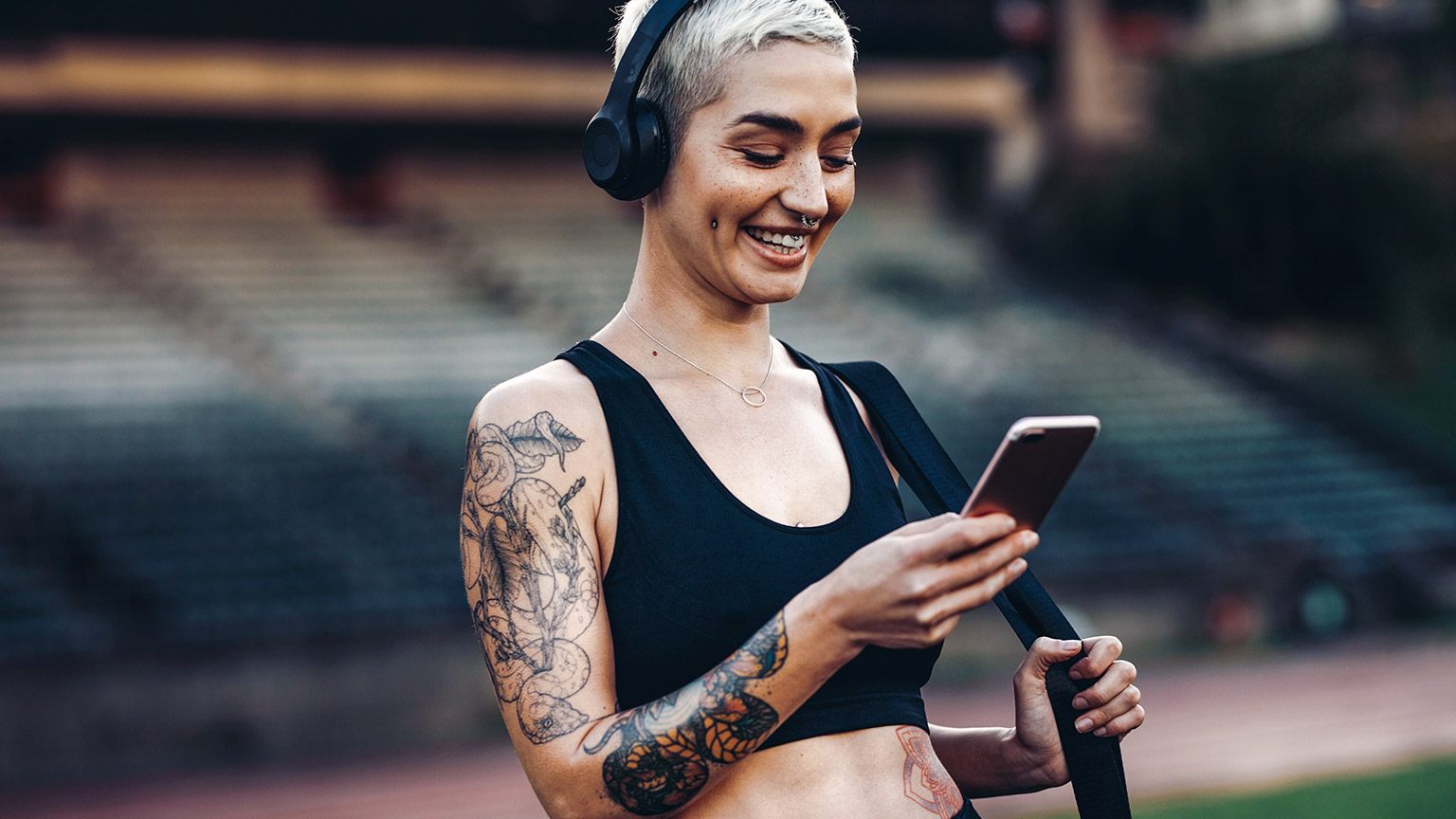 Female outdoors wearing workout gear and looking at mobile phone while smiling