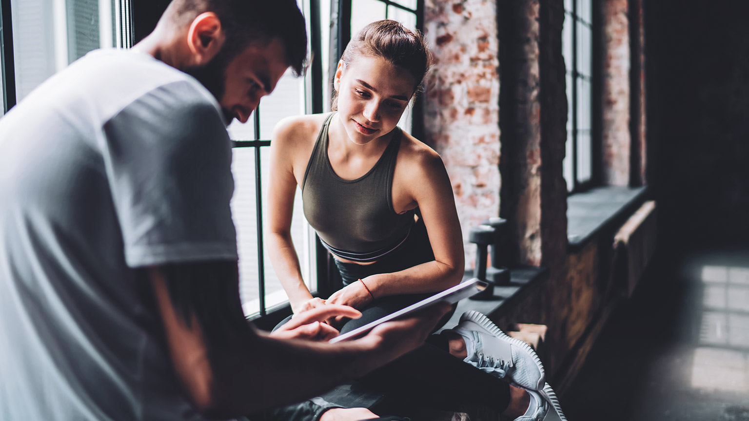 Male trainer showing female client something on a tablet device