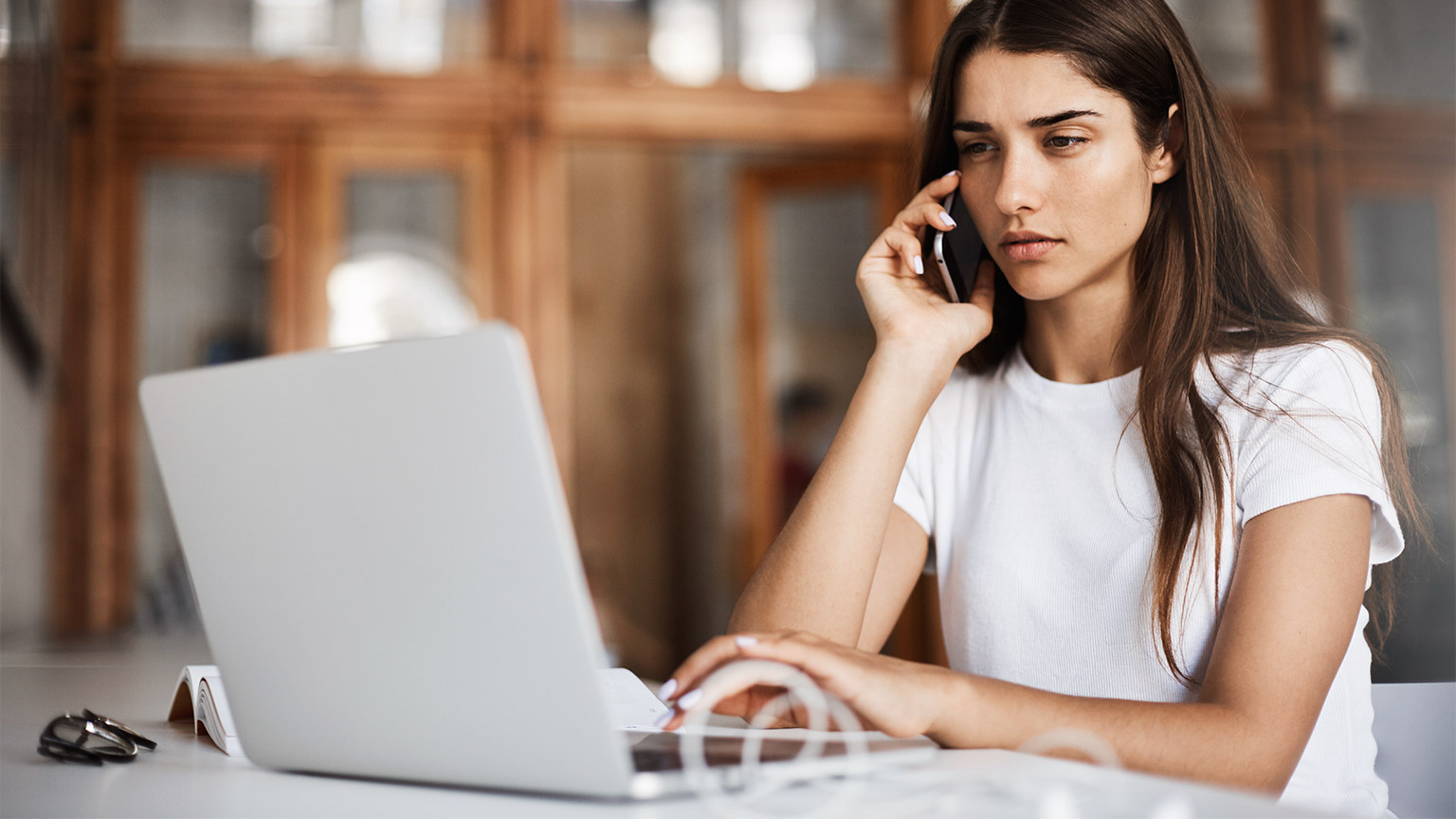 A person on their phone sitting in front of their laptop