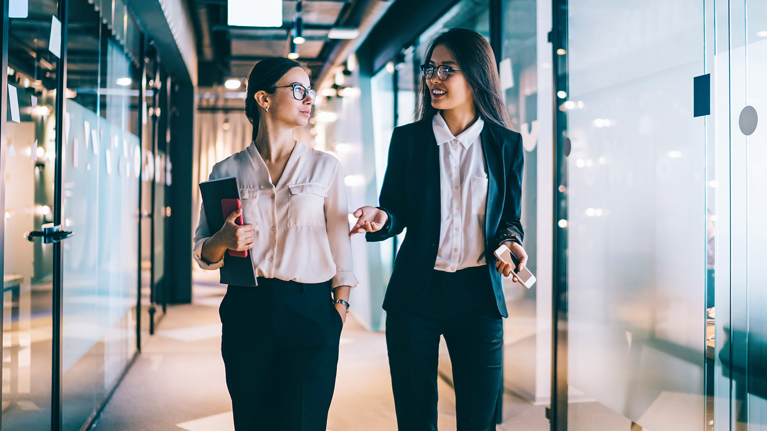 Two female colleagues walking down the hallway of a modern office