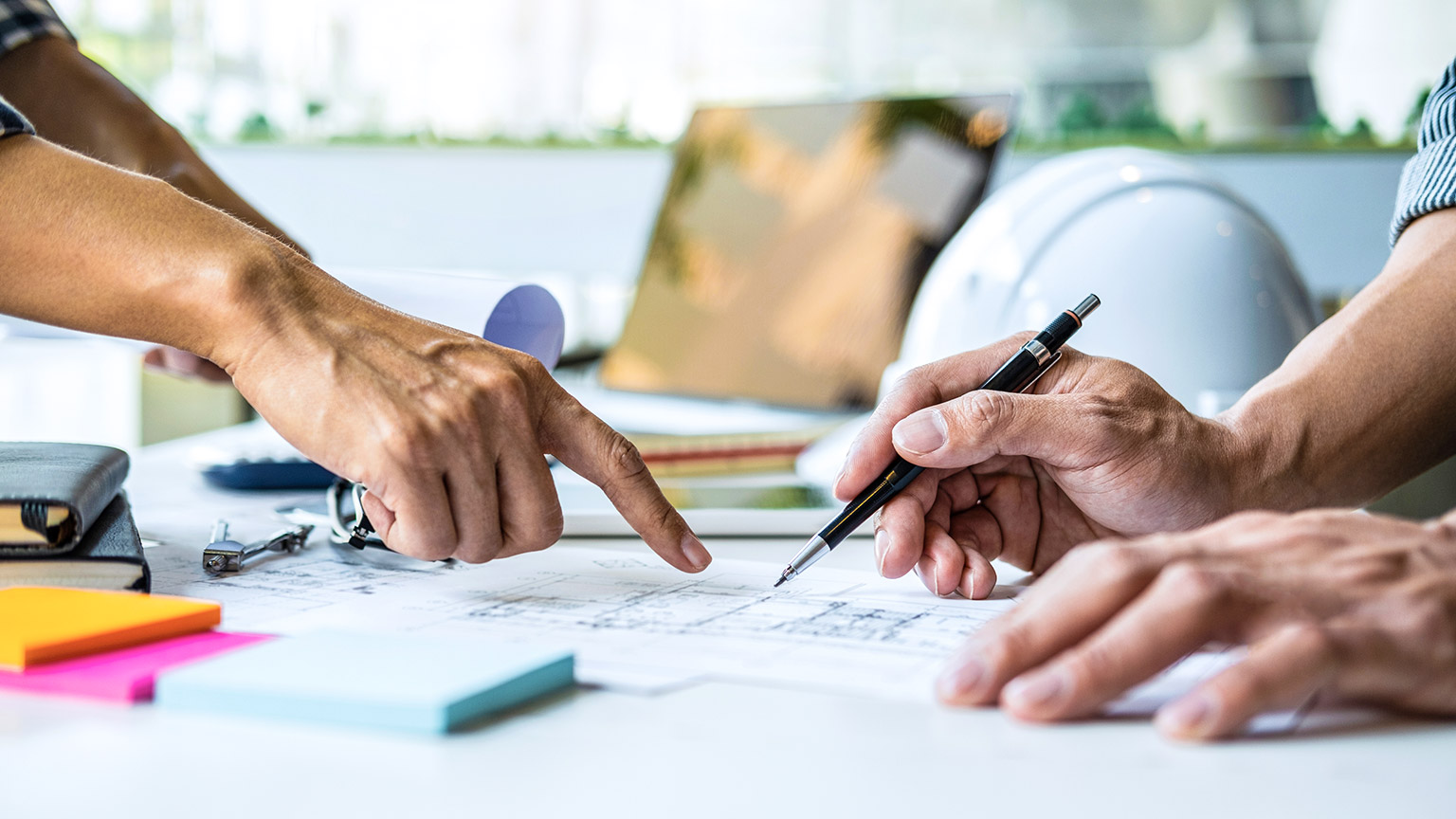 Close view of 2 coworkers looking at a building plan on a desk