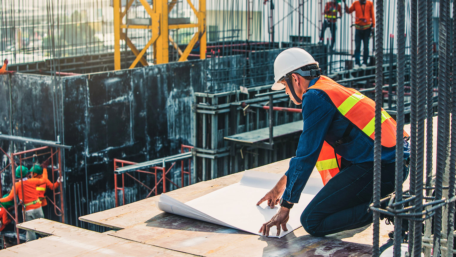 A foreman kneeling down and examining plans on a building site