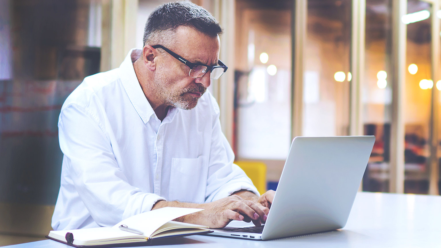 Mature male sitting at desk in office typing on laptop