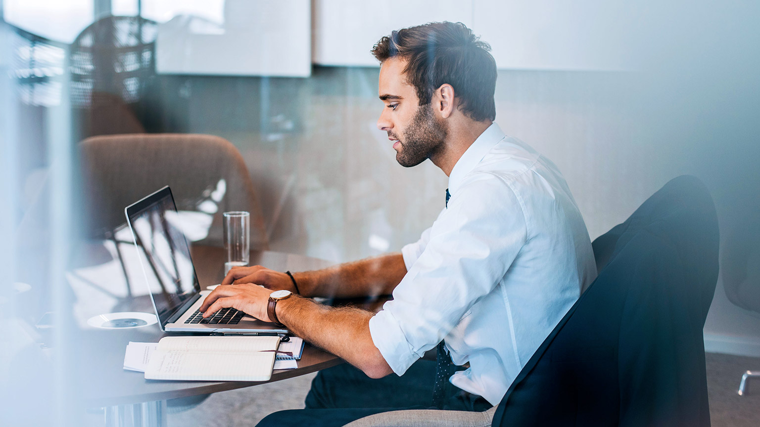 A young accountant sitting at a desk working on a financial report on their laptop