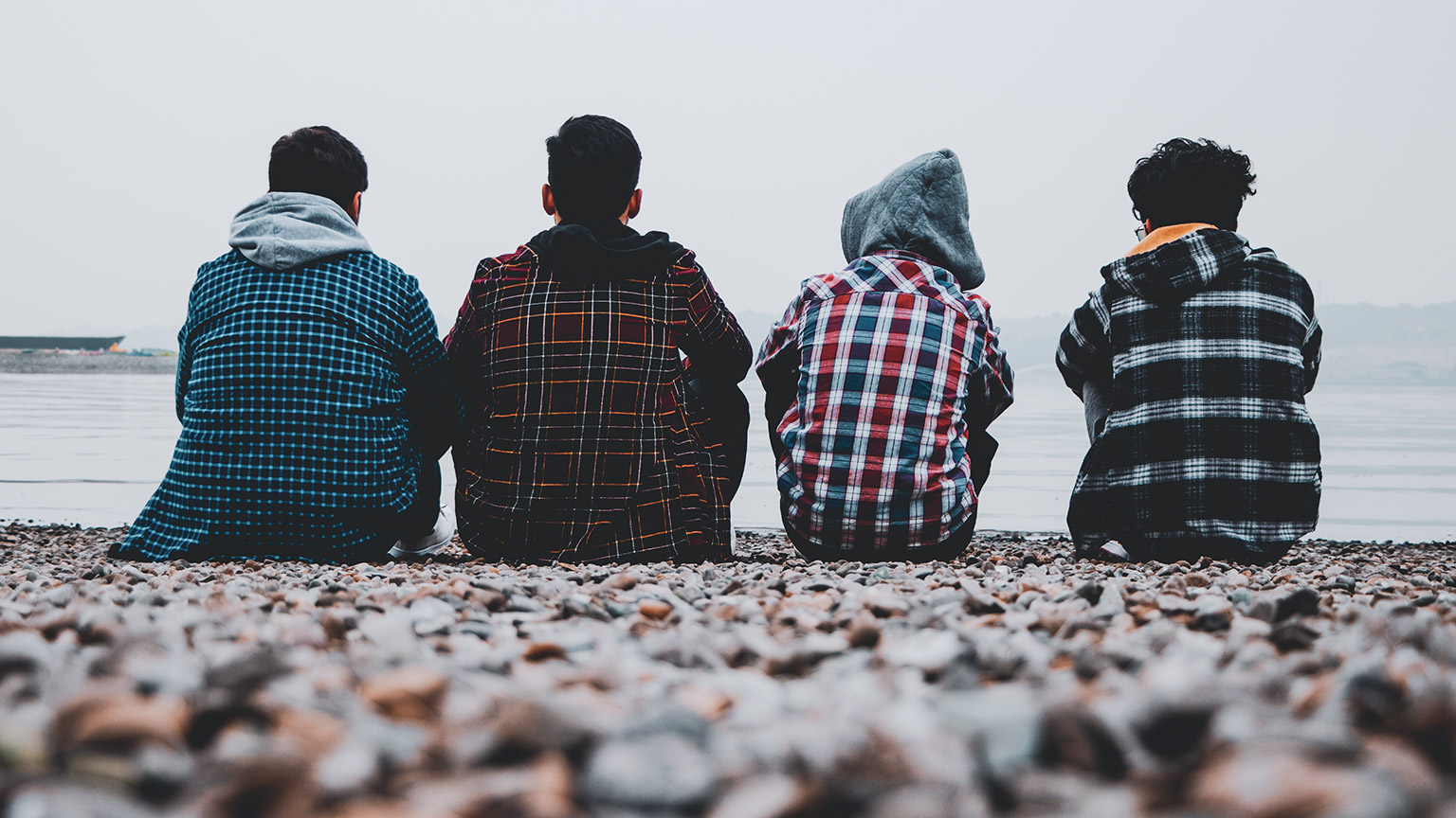 Four teenagers with their backs to the camera, sitting on a beach and looking out at the ocean