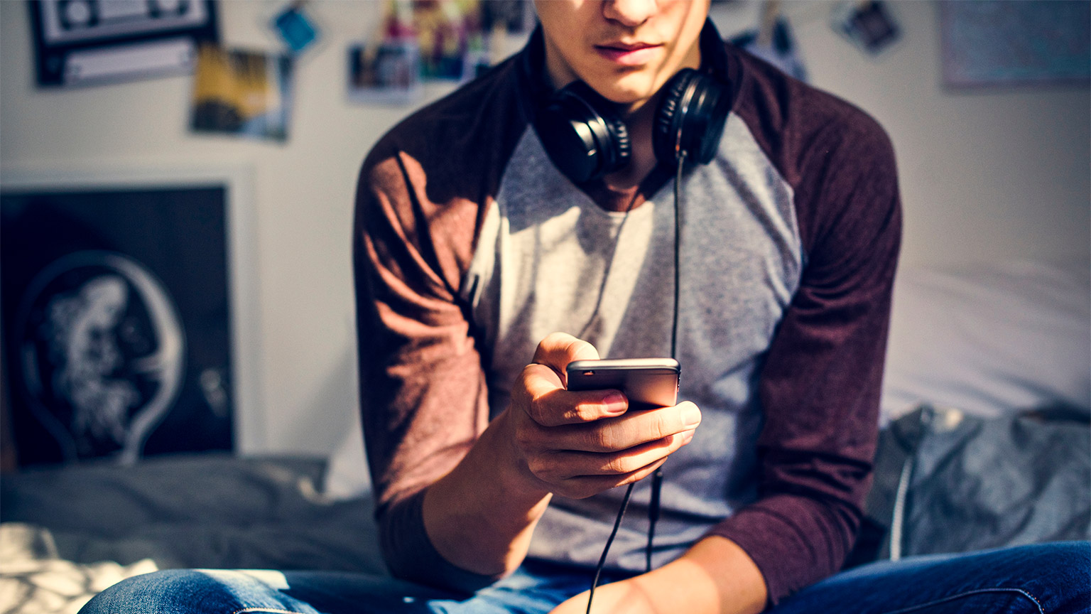 A teenager sitting on their bed, doom-scrolling through social media on their smart phone