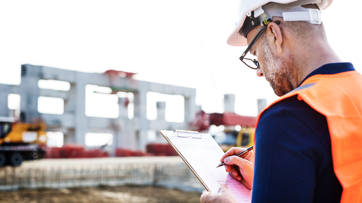 A construction supervisor on a work site doing a safety audit with pen and clipboard in hand