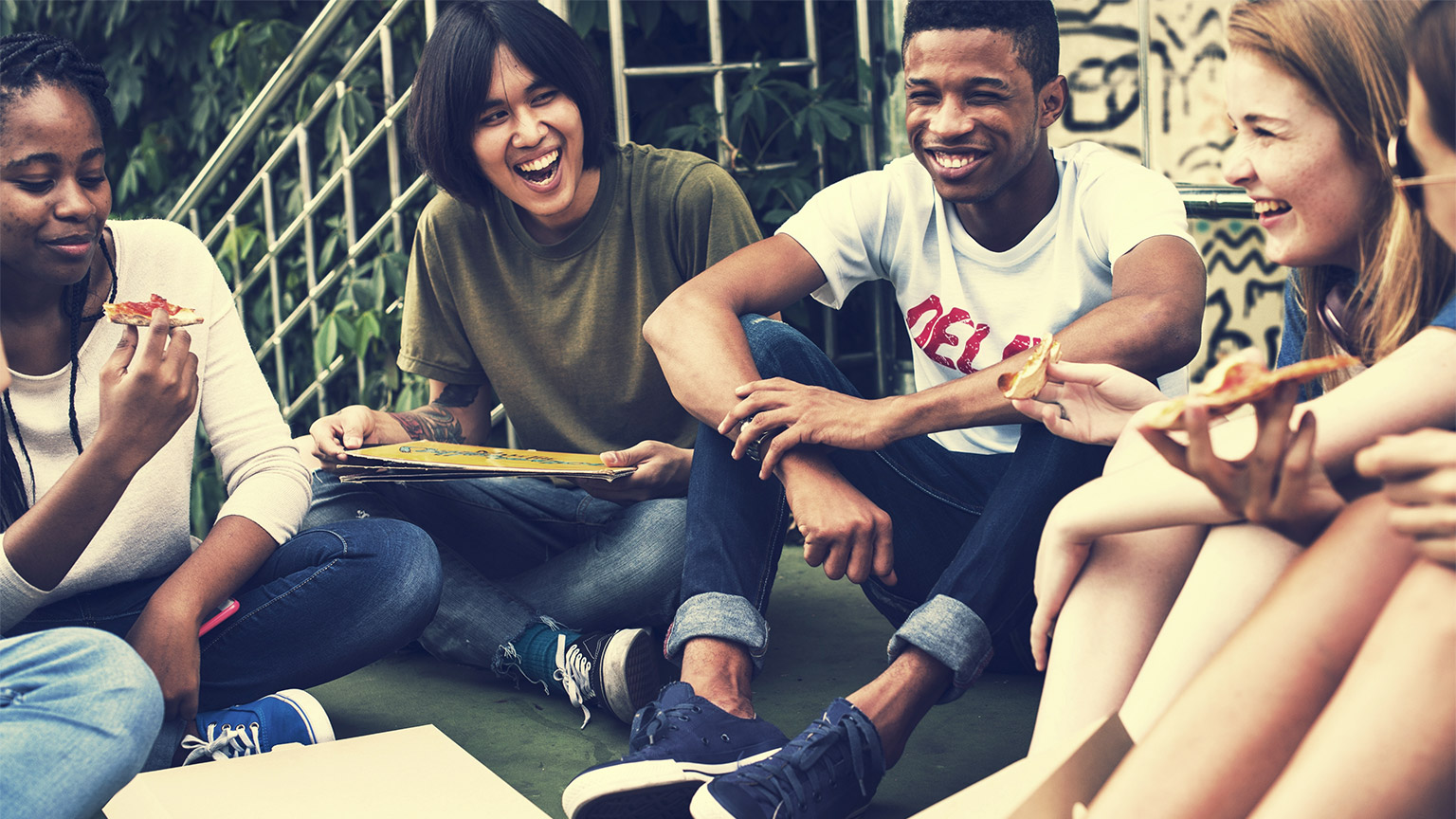 A group of young people sitting together eating pizza