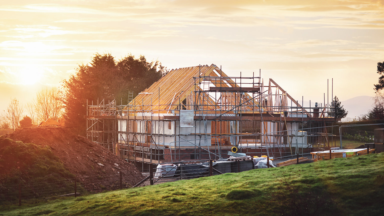 A residential home under construction, in a rural setting at sunrise