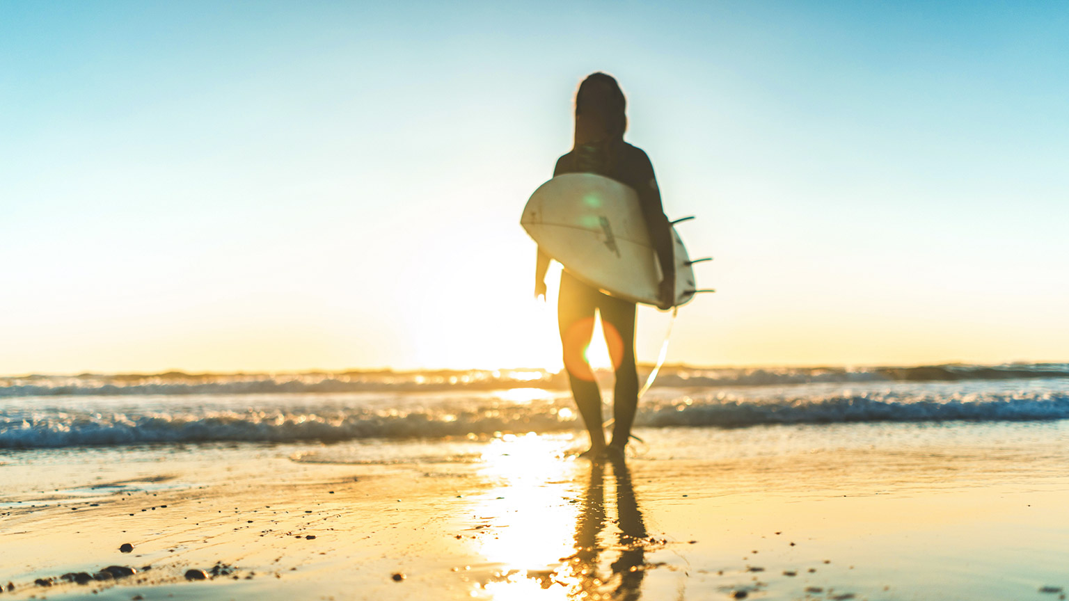 A silhouette of a surfer standing on a beach with a surfboard