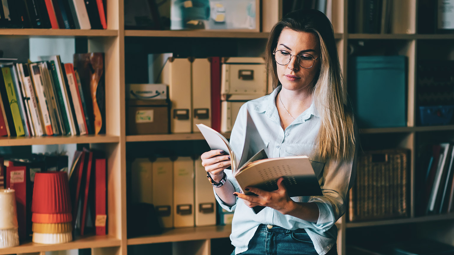 A young professional standing in a library reading reference material