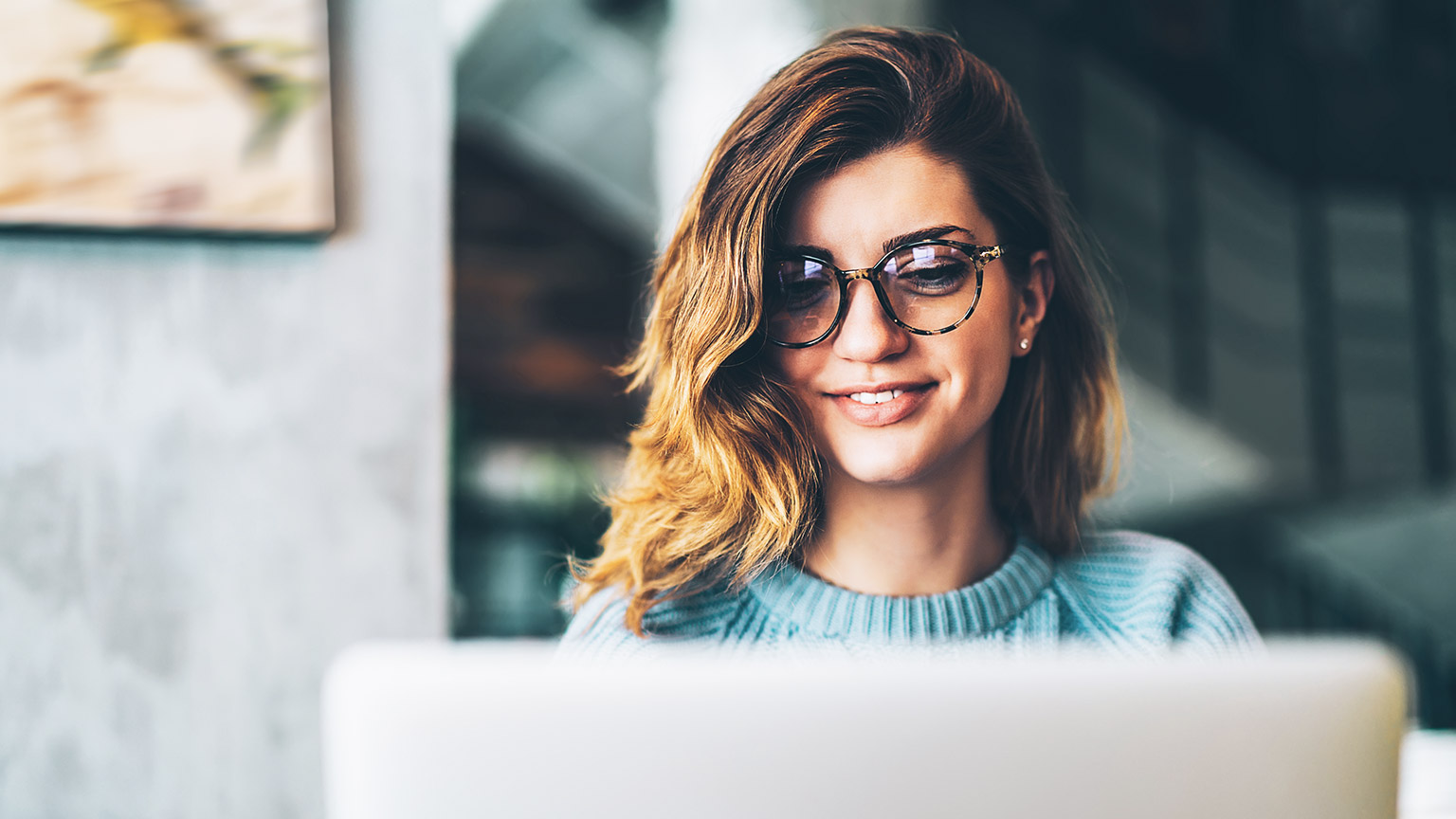 A smiling designer working on a laptop in a casual office environment