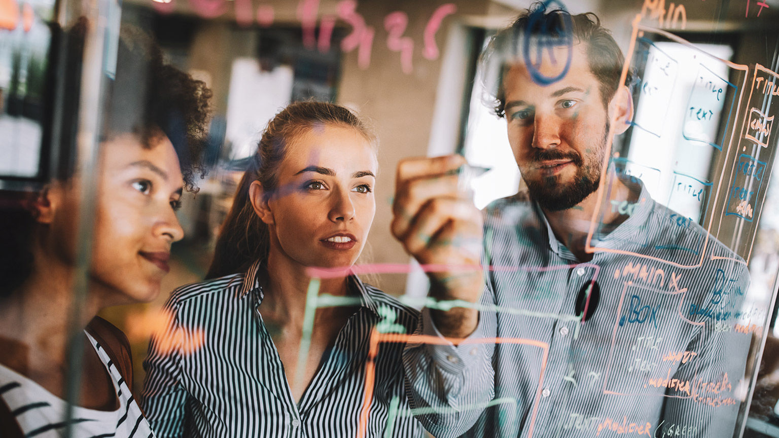 A trio of business colleagues writing out a solution on a glass window