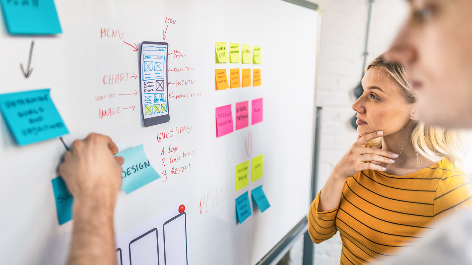 2 designers standing at a whiteboard mapping out UI/UX strategy