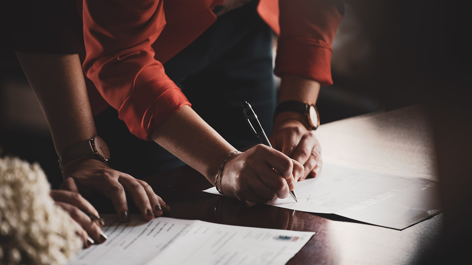 2 business people signing documents on a table