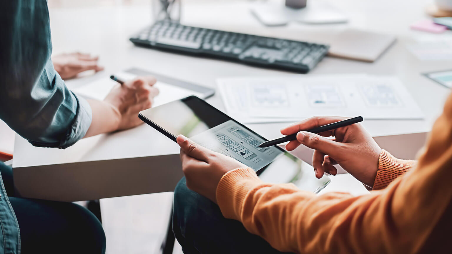 A designer drawing wireframes on a tablet device while a coworker works in the background