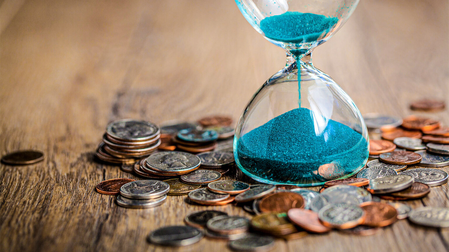 An hourglass nestled among many small-denomination coins