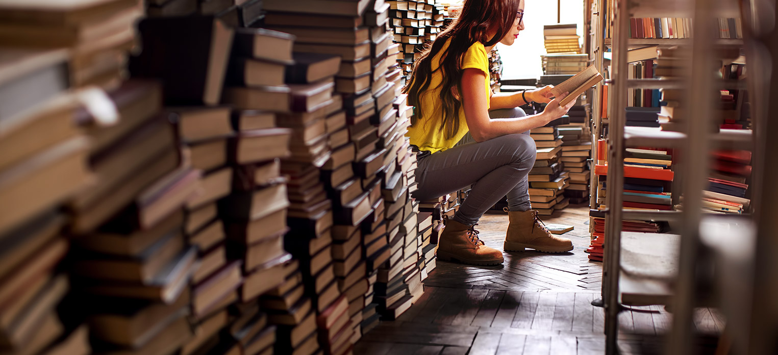 a person reading while sitting on top of stacks of books