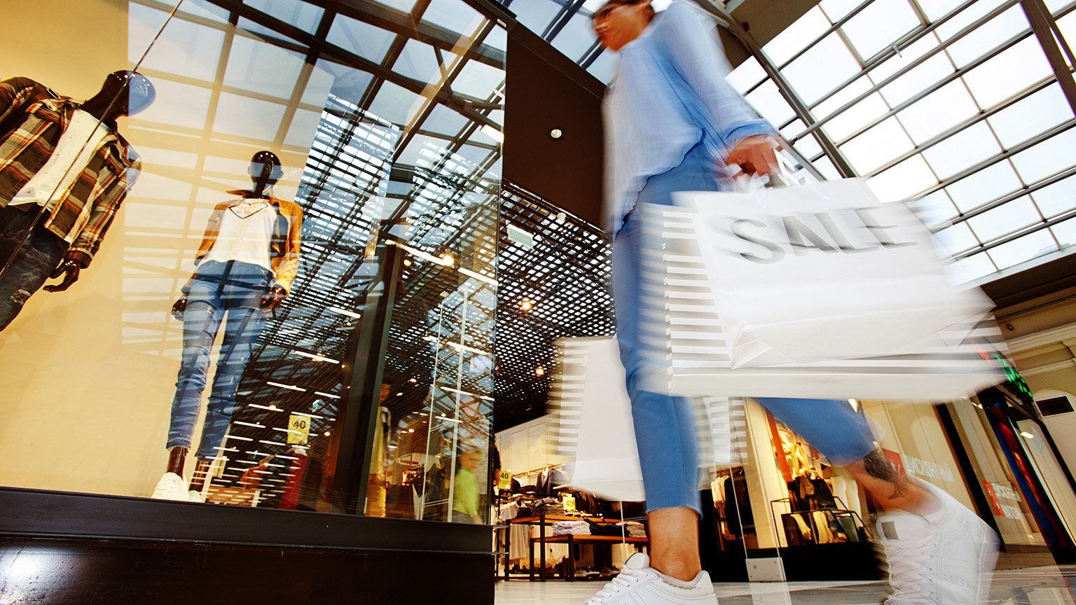 A person with shopping bags walking beside store fronts