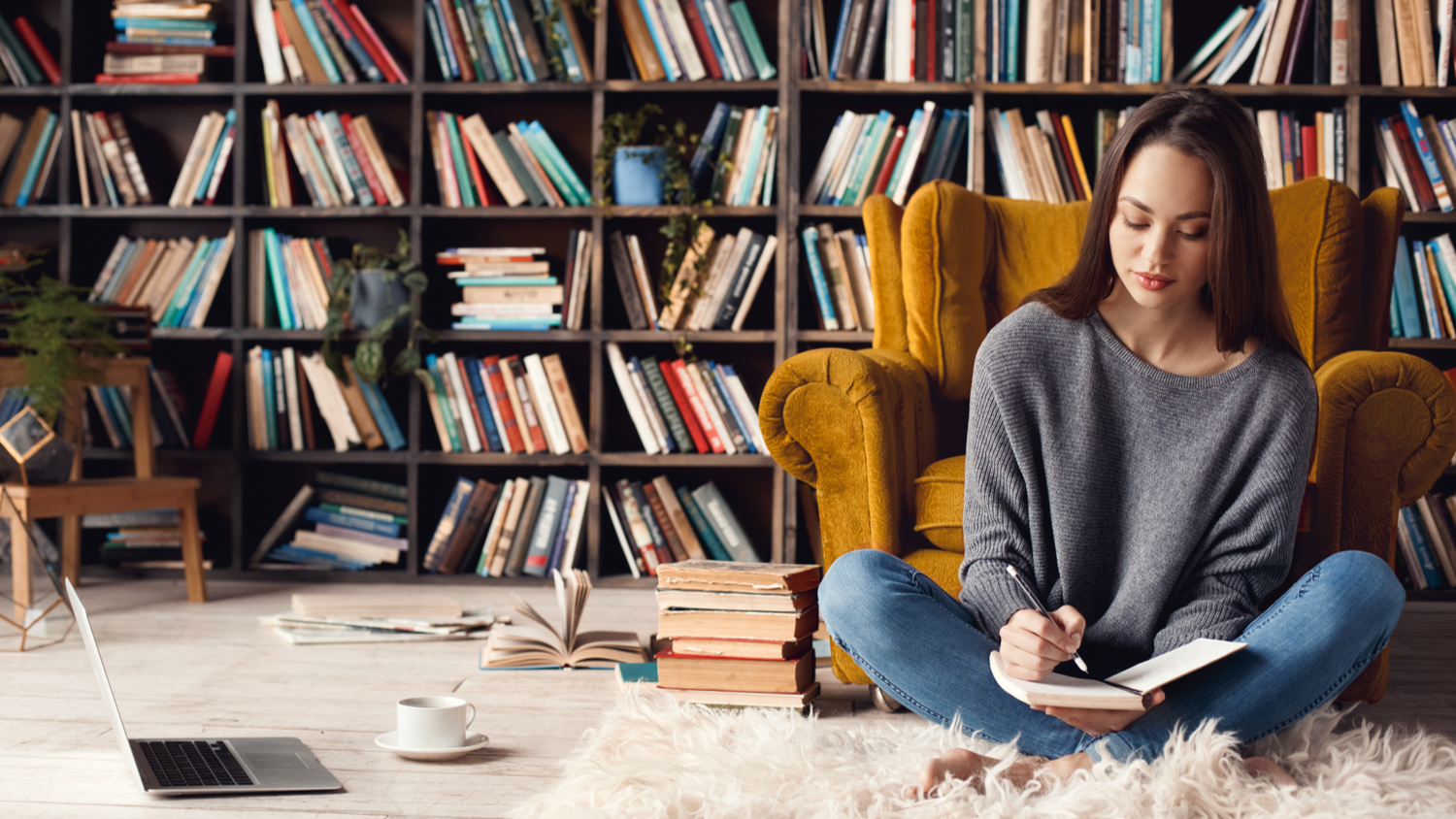 Female uni student in library at home sitting writing notes as she reads an academic journal article