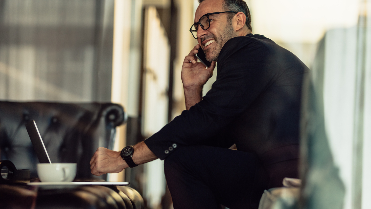 A smiling mature businessman sitting with a coffee talking on mobile phone.