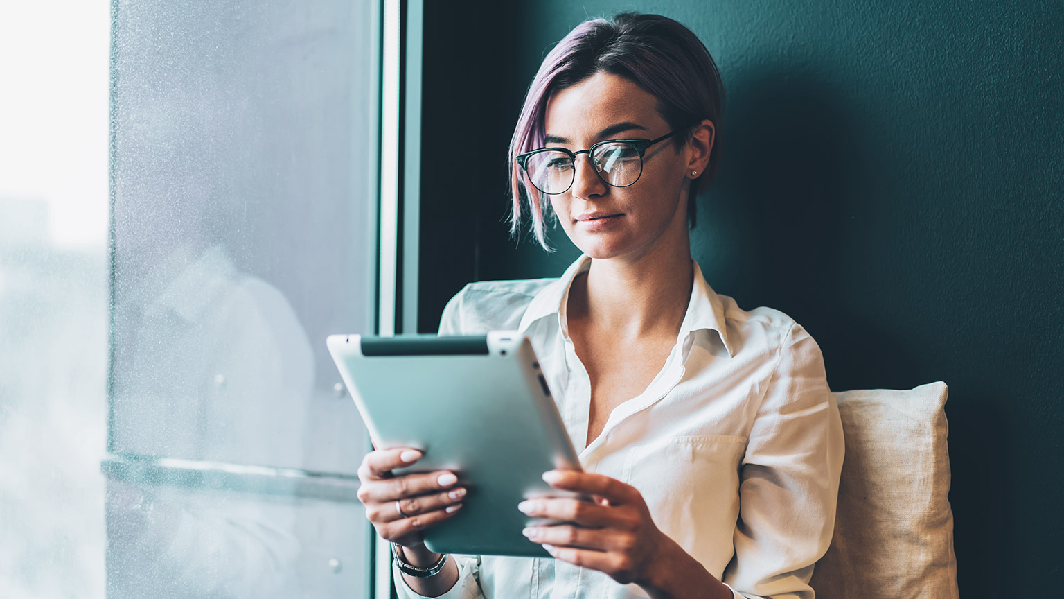 A young professional sitting next to a window engaging with a tablet device