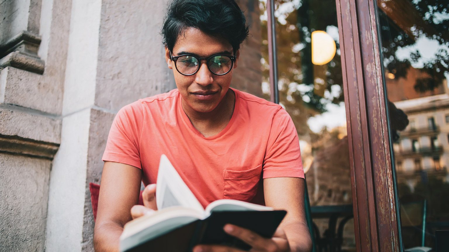 A young student sitting outside a library reading a book