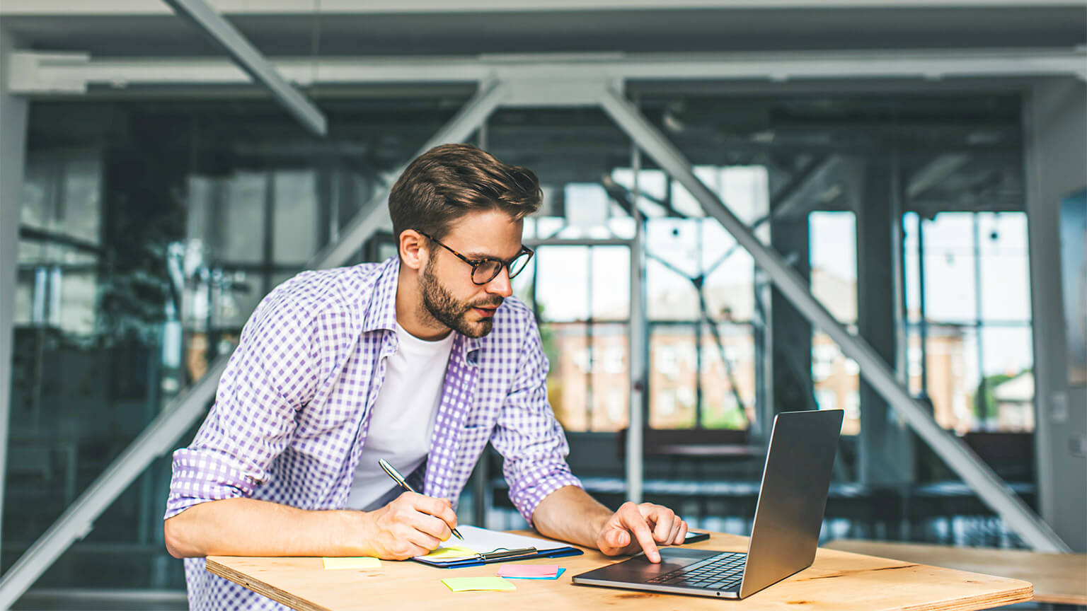 A young professional leaning on a desk, writing down references for some of their research