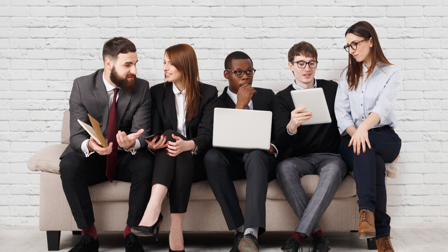 Great team work. Colleagues enjoying successful project, business partners celebrate victory at workplace, sitting on couch against white brick wall background, copy space