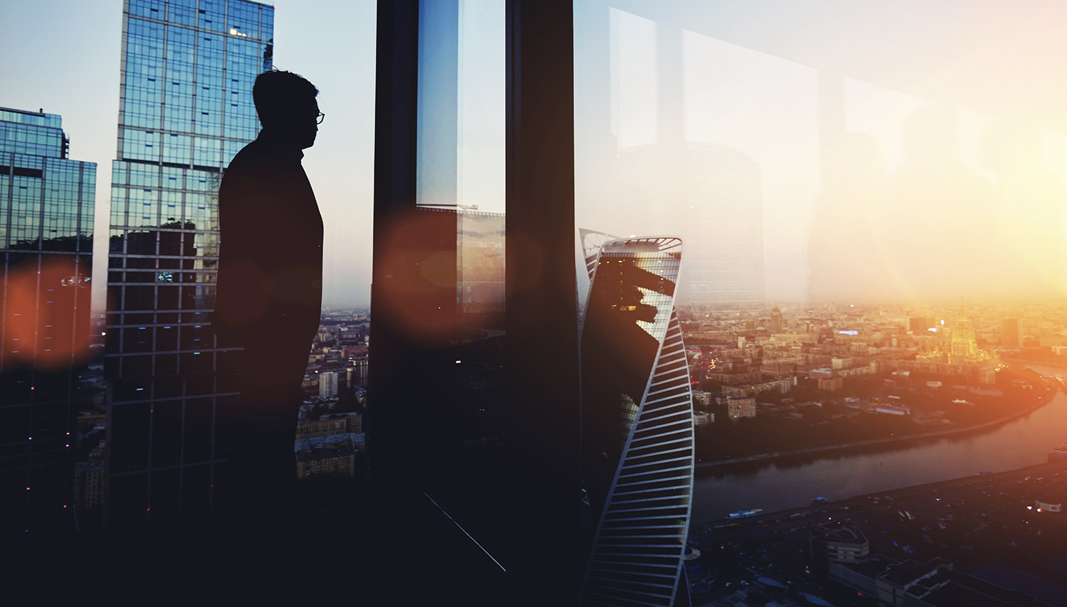 A professional, in deep thought, staring across a city skyline at dusk