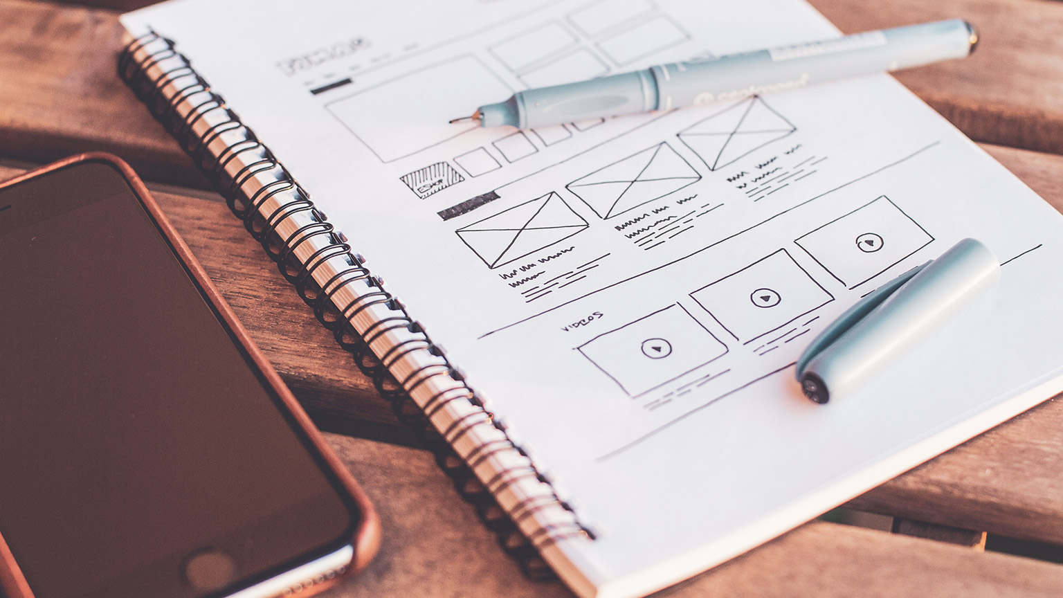 A close view of a notepad and phone on a table- the notepad has UX diagrams on it