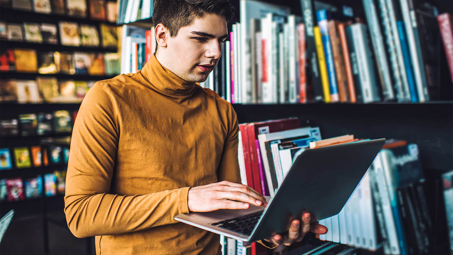 A healthcare worker spending time in the library, absorbing a textbook on their laptop