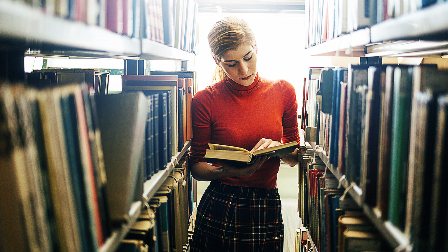 A student absorbing a book about handling animals in the aisle of a library