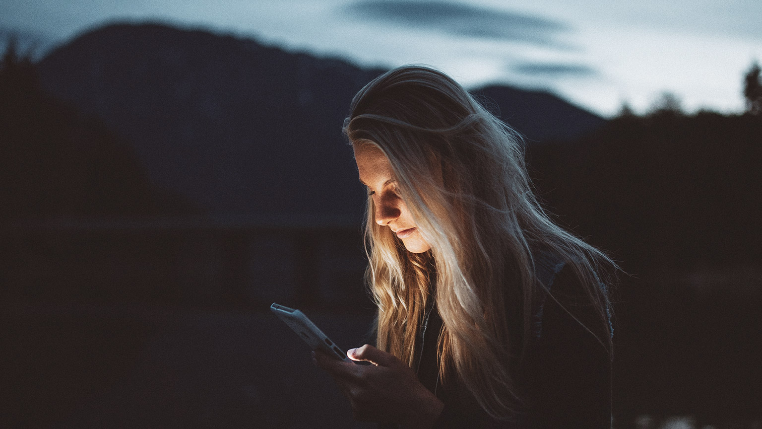 A person illuminated by their mobile phone while sitting in an outdoor location