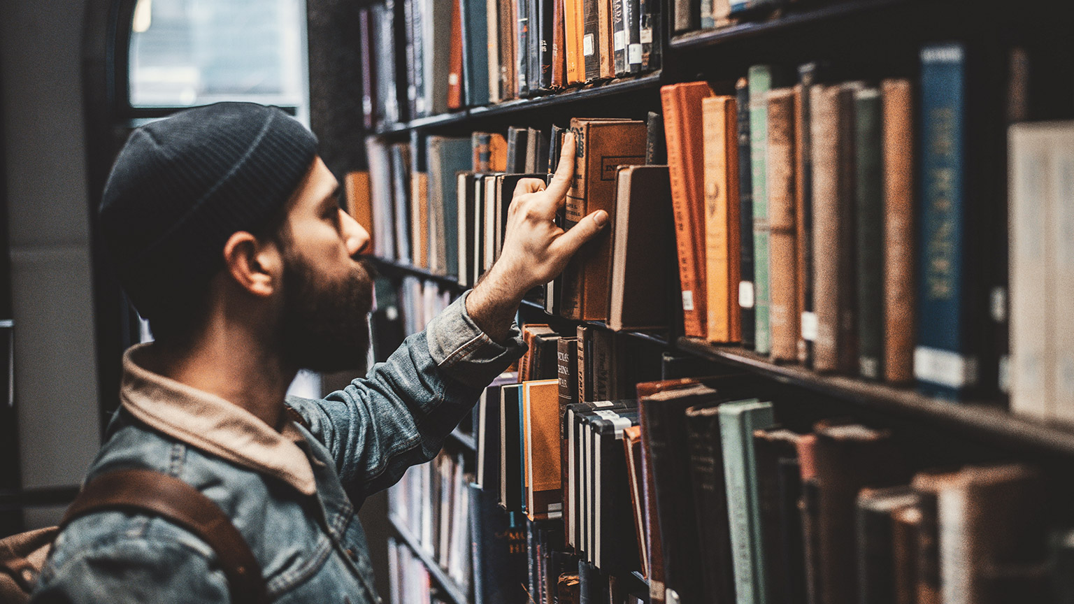 A student grabbing reference materials from the shelf of a library