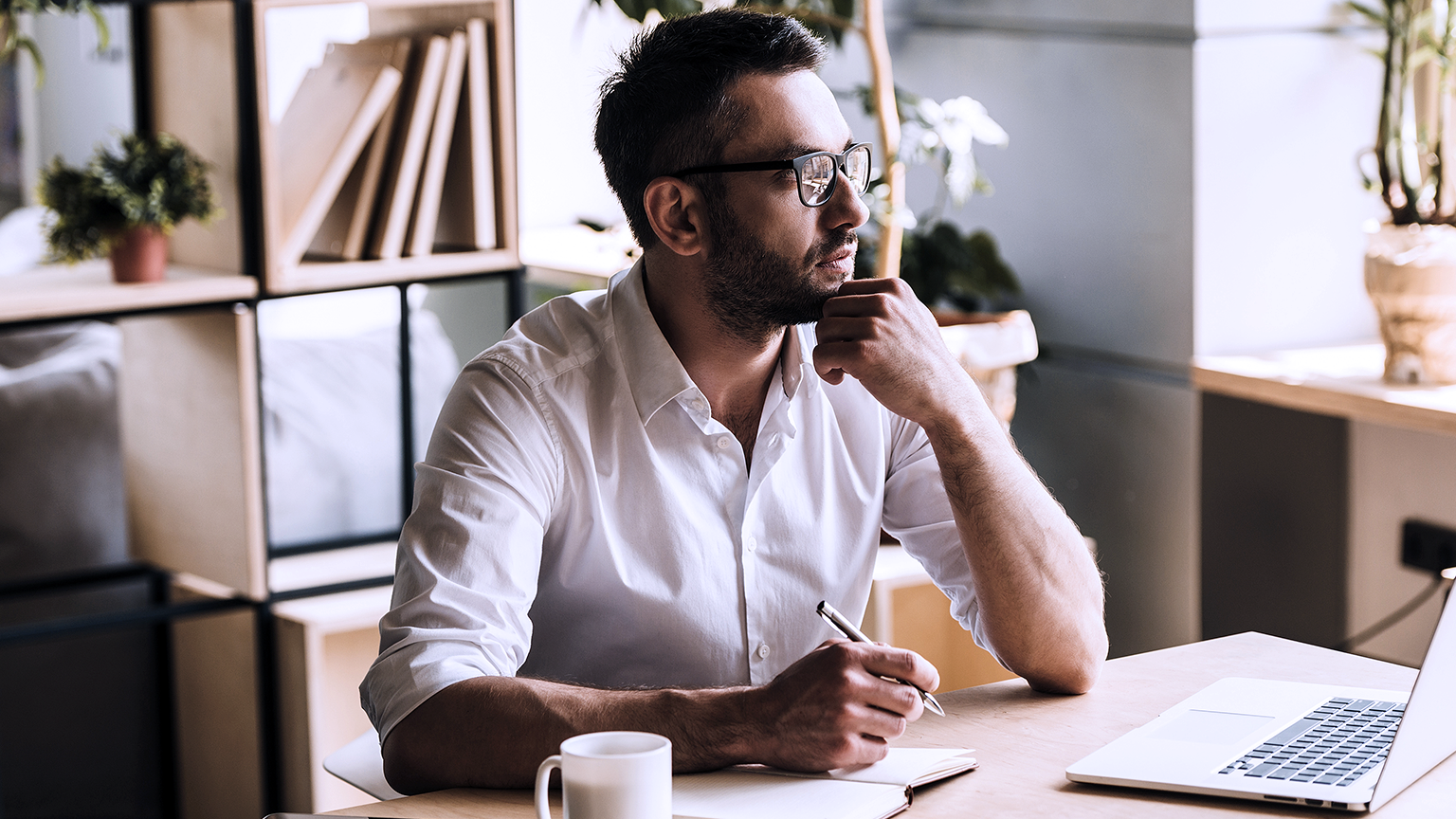 man holding a pen looking away while sitting at his working place