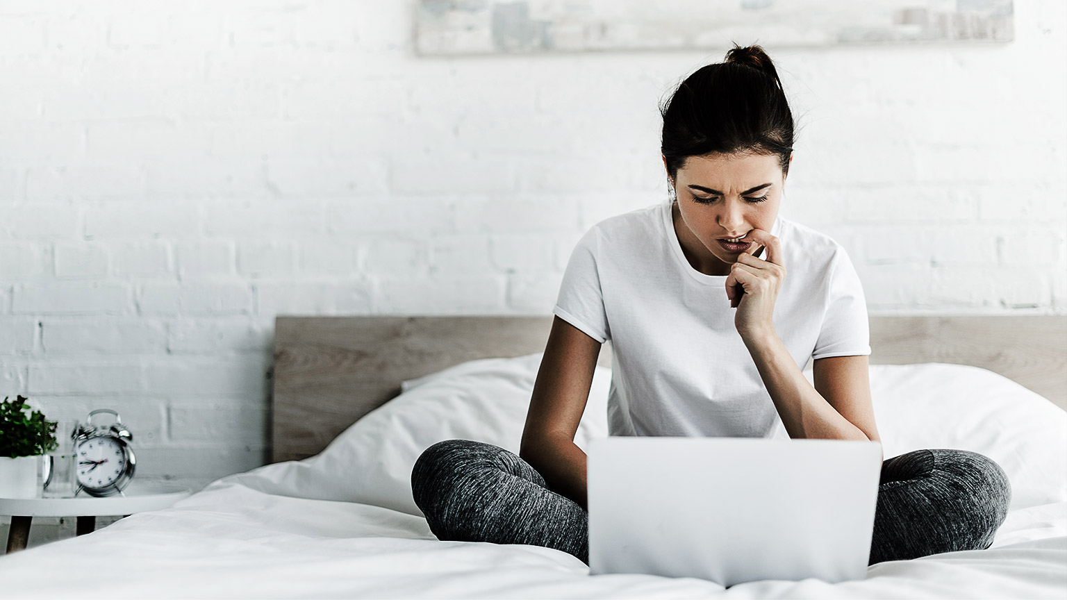 young woman sitting working on a laptop looking puzzled