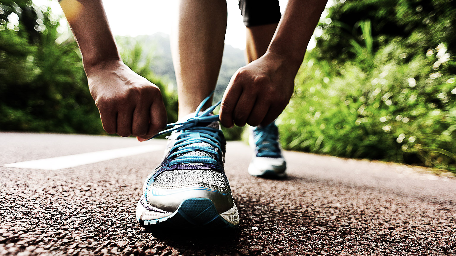 A woman on a track tying her running shoe laces getting ready for a jog. 