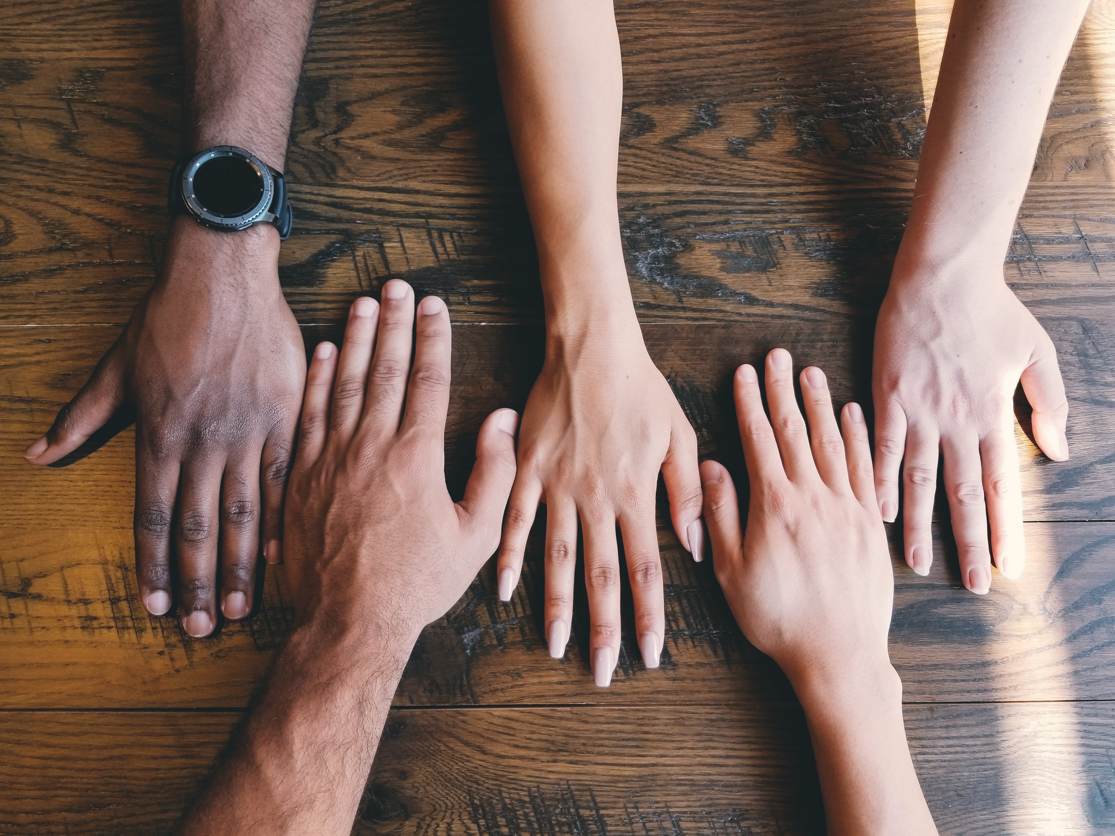 5 different people's hands placed side by side on a background of wooden table