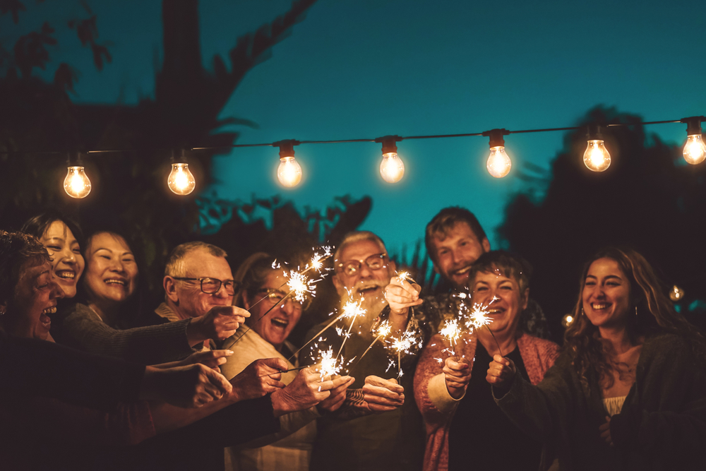 Group of people with different ages and ethnicity, celebrating with sparklers at night outdoors